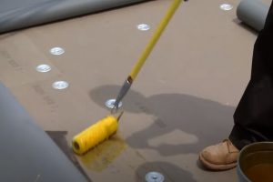 Flat roof sealant being applied by roller with a Kitchener Roofing employee